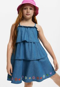 Jeanskleid mit einem geschichteten Design, Rüschenträgern und bunten gestickten Mustern von Blumen, Herzen und Friedenssymbolen am Saum.