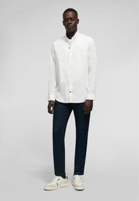 Witte overhem shirt met een kraag, gecombineerd met donkerblauwe jeans en witte sneakers. Het shirt heeft een knoopsluiting en lange mouwen.