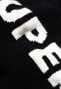 Tessuto nero a maglia con lettering bianco audace. La texture è morbida e il design presenta bordi netti e contrasti tra i colori.