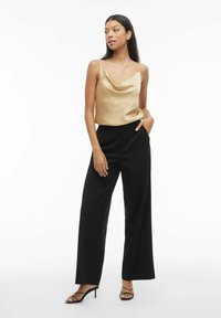 Kergelt kuldne satiinist kaelus-top, mis on paaritatud kõrge vöökohaga mustade laiade pükstega. Mudel kannab musti kontsakingi. Puhtne, minimaalne taust.