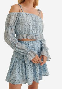 Blå blomster to-delt sæt med en cropped off-shoulder top med pufærmer og en flared nederdel med flæser. Letvægtsstof.