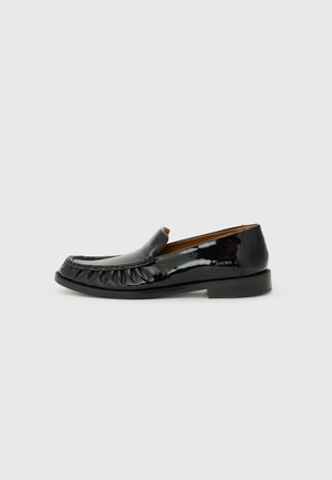Mocassins en cuir verni noir avec un bout rond, des détails froncés à l'avant et un petit talon. La semelle est plate et lisse.