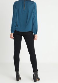 Teal, långärmad blus med en nyckelhålsrygg, slät textur, och kombineras med åtsittande svarta jeans och ankelstövlar.
