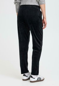 Sorte cordfløyelsbukser med rett passform, ribbet tekstur, elastisk midjebånd og sidelommer, kombinert med hvite joggesko.