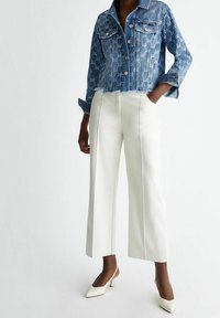 Denimjacka med en strukturerad blå design, två bröstfickor, kort längd och fransad fåll, i kombination med högmidjade vita vida byxor.