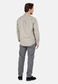 Light gray long-sleeve shirt with a button-down collar, back pleat detail, and subtle logo. Paired with gray trousers and black shoes.