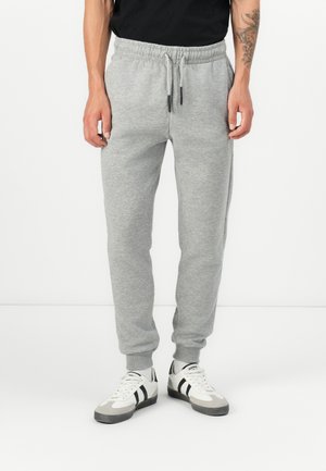 Grey cotton sweatpants with an elastic waistband and drawstring. Tapered fit with ribbed cuffs. Paired with white sneakers featuring black accents.
