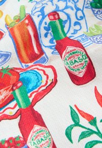Tessuto a fantasia che mostra bottiglie rosse di salsa Tabasco, peperoncini rossi, un pomodoro, un guscio d'ostrica e un bicchiere con verdure su uno sfondo bianco e blu.