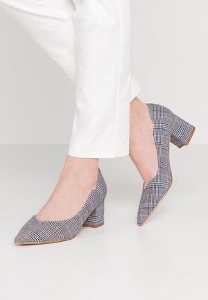 Zapatos de tacón alto de cuadros grises con punta afilada y lados recortados. Presentan una tela texturizada con acentos en rosa y negro, sobre un tacón bloque.