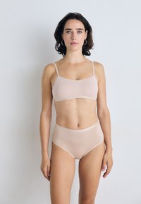 Lys beige sømløs bralette og høy midje undertøy sett. Myk, elastisk stoff med tynne stropper og en jevn tekstur. Ingen mønstre.