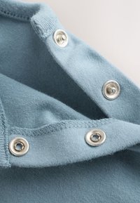 Close-up of light blue fabric with silver snap fasteners partially opened, showing stitching details on soft material.
