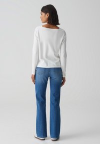 Witte long sleeve top met een vierkante halslijn aan de achterkant, gecombineerd met blauwe flared jeans. De stof lijkt soepel en casual, met eenvoudige stiksels.