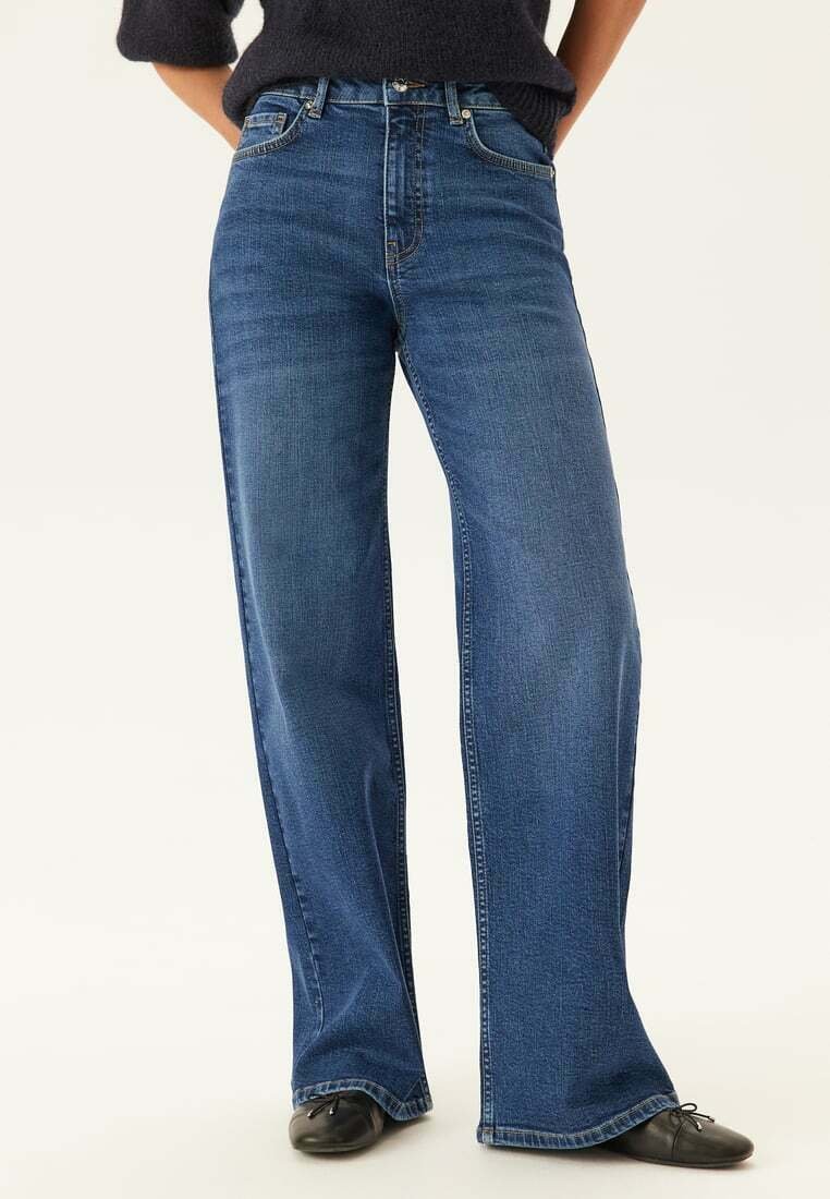 Bredbenta blå jeans i denim, med hög midja, subtil blekning och klassisk femficksdesign. Svarta skor fulländar outfiten.