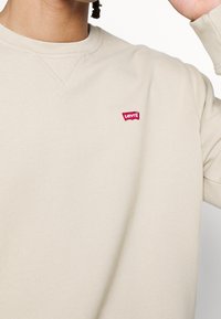 Felpa beige con collo rotondo, caratterizzata da un piccolo logo rosso di Levi's sul petto. Tessuto morbido con maniche inserite.