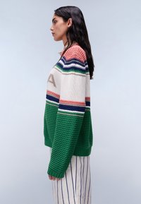 Gehaakte pullover in crème, groen en roze met horizontale strepen. Kenmerkt zich door een gestructureerd lijf, geribbelde zoom en subtiele logodetail.