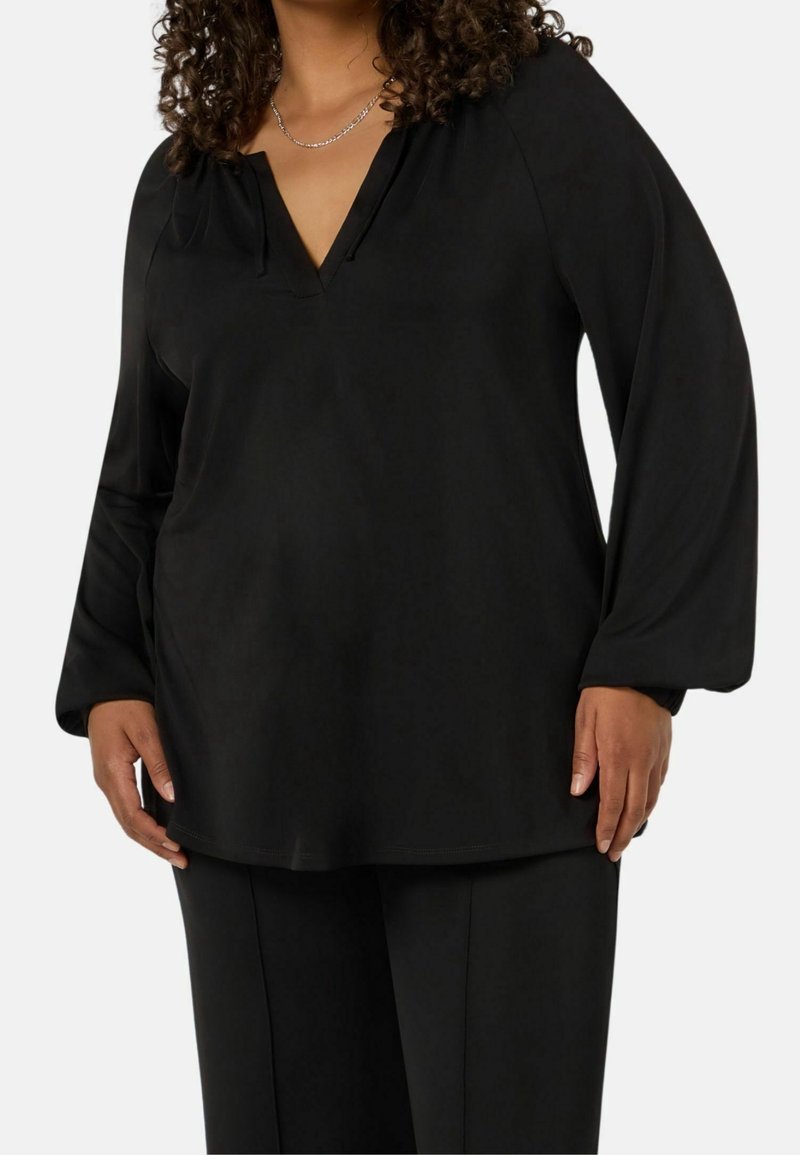 Svart långärmad topp med V-ringning och avslappnad passform, i slät tyg och minimalistisk design. Kombinerad med matchande byxor.