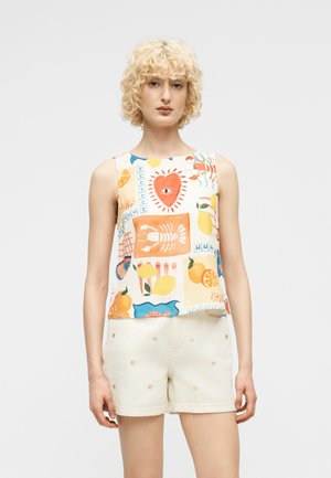 Persona rubia con cabello rizado que lleva una camiseta sin mangas con estampados coloridos de frutas y langostas, y pantalones cortos crema con pequeños corazones bordados.