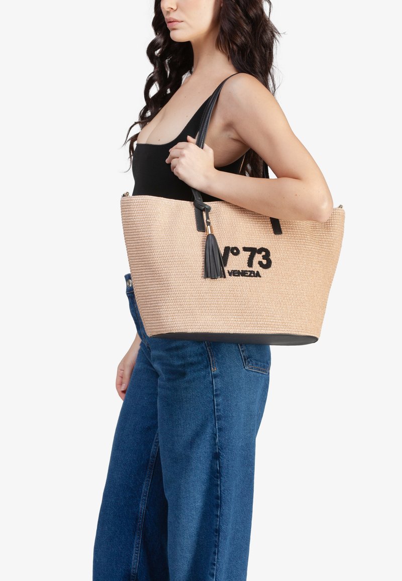 Borsa a spalla di paglia color paglierino con dettagli neri, dotata di chiusura a zip e nappina decorativa. Ha un design spazioso e una grafica testuale audace.