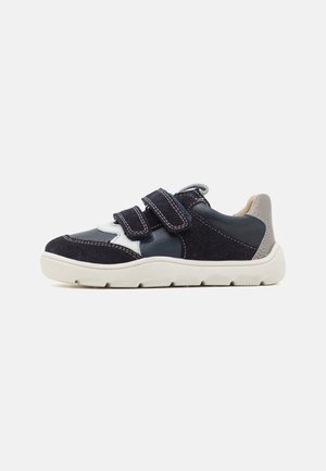 Shoe de camurça preto e azul-marinho com tiras de velcro, sola branca e acabamentos cinzentos. Apresenta painéis contrastantes e detalhes de costura na parte superior.