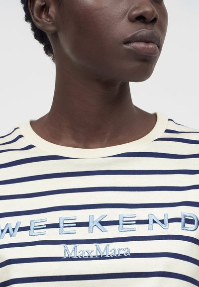 Κοντινό πλάνο ενός ατόμου που φοράει μία λευκή και ναυτικό ριγέ μπλούζα με κεντημένο το "WEEKEND MaxMara" στο στήθος.