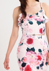 Top de flores corto con tirantes con volantes, que presenta tonos de rosa, blanco y verde oscuro. El material tiene una textura suave, adornada con grandes patrones de flores.