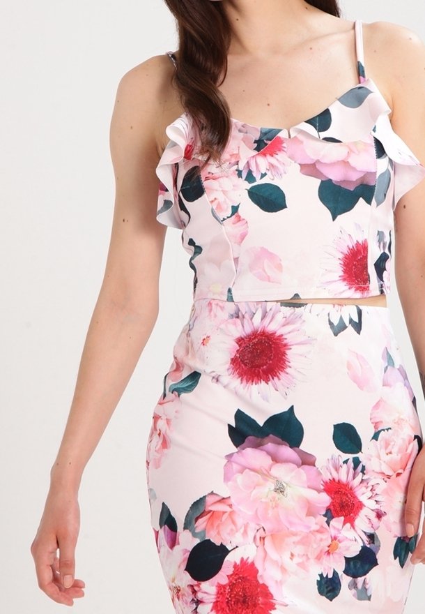 Top de flores corto con tirantes con volantes, que presenta tonos de rosa, blanco y verde oscuro. El material tiene una textura suave, adornada con grandes patrones de flores.