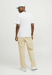 Hvid t-shirt, beige cargo bukser med lommer, og lyseblå kasket. Modellen står med ryggen til, hvilket viser den afslappede pasform og glatte materiale.