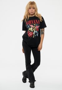 Black graphic t-shirt featuring a colorful Nirvana design, paired with high-waisted black flared jeans and black ankle boots.