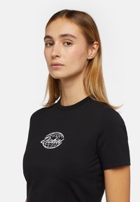 Camiseta negra de manga corta con cuello redondo. Presenta un diseño gráfico blanco que se asemeja a un globo. Fabricada en tejido de algodón.