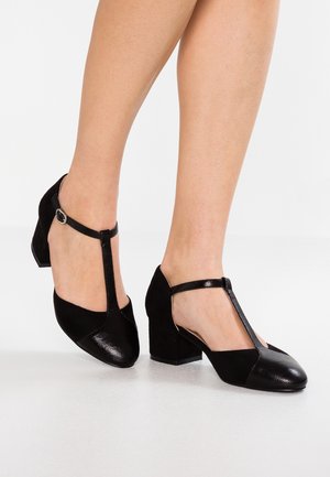 Czarne buty na obcasie z zapięciem T, wykonane z teksturowanych i gładkich materiałów. Posiadają kwadratowy obcas i detal z klamrą wokół kostki.