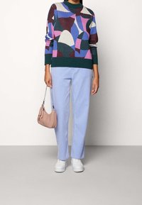 Neulepaita, jossa on monivärisiä abstrakteja kuvioita, yhdistettyinä vaaleansinisiin suoriin farkkuihin. Asusteina pieni vaaleanpunainen käsilaukku ja valkoiset tennarit.