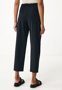 Svarta, korta byxor med elastisk midja, i en slät textur och med sidofickor, kombinerade med platta svarta sandaler.