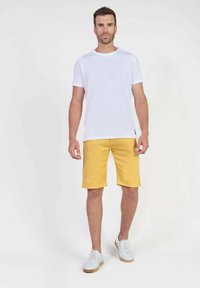 T-shirt blanc à manches courtes associé à un short jaune vif jusqu'aux genoux et des baskets blanches. Design simple, coupe décontractée, sans motifs ni logos.