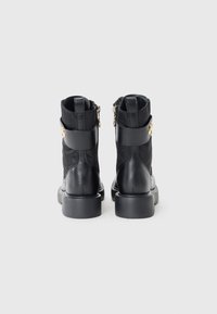 Black leather ankle boots with a chunky heel, featuring a zip closure and a decorative strap with gold hardware. Textured surface.