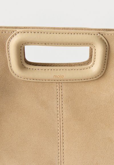 Sac à main en daim beige avec poignée découpée rectangulaire et bordure en cuir cousue, portant le nom de la marque "maje" embossé sous la poignée.