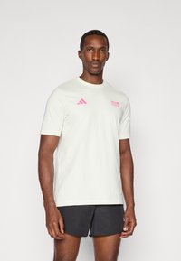 Tricou athletic de culoare verde deschis, cu mâneci scurte, cu logo și text Adidas roz, decolteu rotund, fabricat dintr-un material moale, croială lejeră, potrivit pentru sport.
