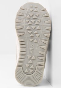 Sole di sneakers bianche in materiale gommoso, con superficie testurizzata, motivo a rilievo triangolare e logo "Fila" impresso.