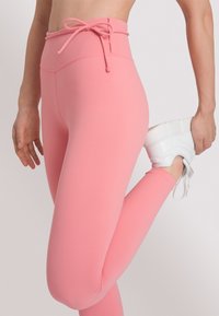 Hooggetailleerde roze leggings met een trekkoord in de taille, een zachte textuur en een slimfit ontwerp, gecombineerd met een witte sneaker.
