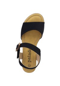 Czarne zamszowe sandały z krzyżującymi się paskami, regulowanym paskiem wokół kostki i okrągłą metalową klamrą. Wyściółka z amortyzacją z beżowymi detalami. Płaska pięta.