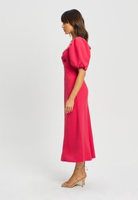 Abito midi con maniche a sbuffo in tessuto rosa brillante, caratterizzato da un corpetto aderente e una gonna fluente, abbinato a sandali alti con tacco a strappo color beige.