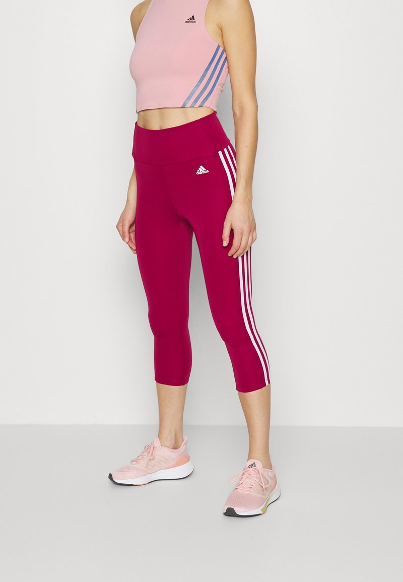 Tætsiddende lyserød crop top med blå striber, parret med højtaljede, knælange burgunder leggings med hvide sidestreger. Lyserøde sportssko.