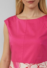 Fuchsia mouwloze top met een ruime halslijn, voorzien van een gladde textuur en een naaddetail aan de voorkant, gecombineerd met een ondergedeelte met een bloemenpatroon.