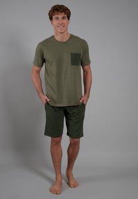 Camiseta de algodón verde oliva con un bolsillo frontal, combinada con pantalones cortos a juego. La tela es suave, presenta un corte holgado y un diseño sencillo.