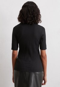 Schwarz geripptes Oberteil mit kurzen Ärmeln, das mit vertikalen Streifen und einer taillierten Passform versehen ist, kombiniert mit einem eleganten schwarzen Lederrock.