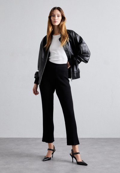 Black leather bomber jacket, white long-sleeve shirt, black ribbed trousers, black pointed heels; smooth textures, fitted silhouette, minimal style.