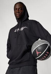 Sort hættetrøje med en frontlomme og et grafisk design på brystet, parret med en sort og grå basketball med et rødt logo.