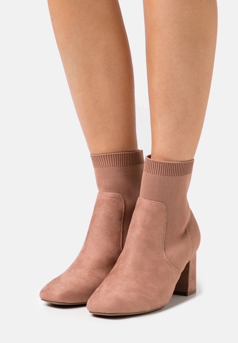 Stivaletti in suede rosa polveroso alti fino alla caviglia, con risvolti a costa in lavorazione a maglia e tacchi a blocco, indossati su gambe scoperte.