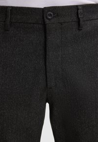 Pantaloni in denim nero con superficie testurizzata, chiusura a bottone discreta e passanti per cintura standard, dal design slim-fit.