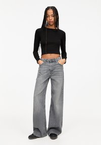 Schwarzes, kurzes Langarmshirt in Kombination mit weit geschnittenen, ausgewaschenen grauen Jeans. Der Stoff ist Denim mit einer glatten Textur und ohne sichtbare Muster.
