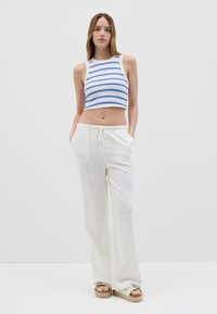 Top de tirantes recortado con rayas azules sobre fondo blanco, combinado con pantalones blancos holgados que presentan una cinturilla elástica y bolsillos.